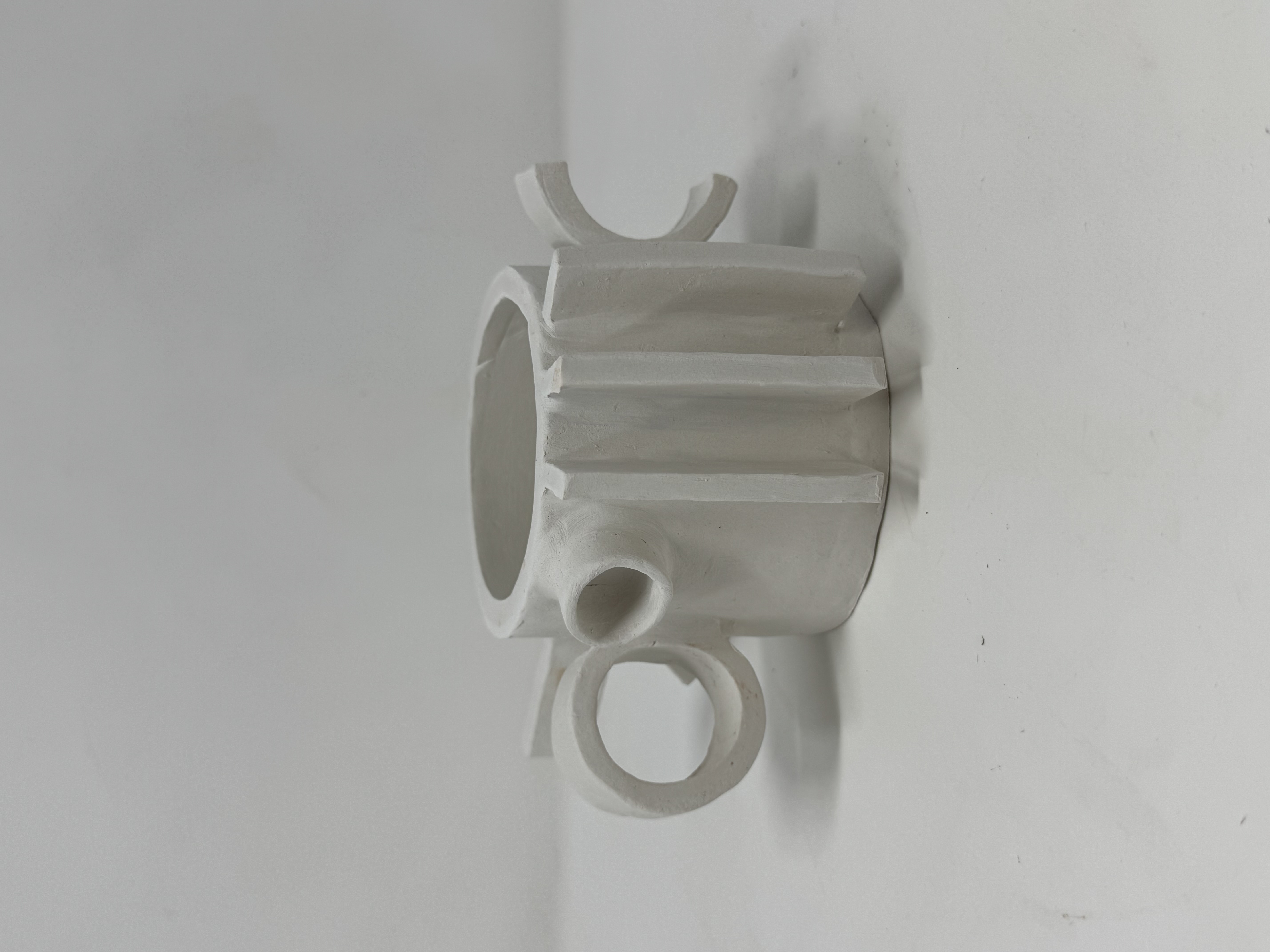 A brutalist-style ceramic mug in a matte white glaze, with a sculpted ribbed body and looped handles